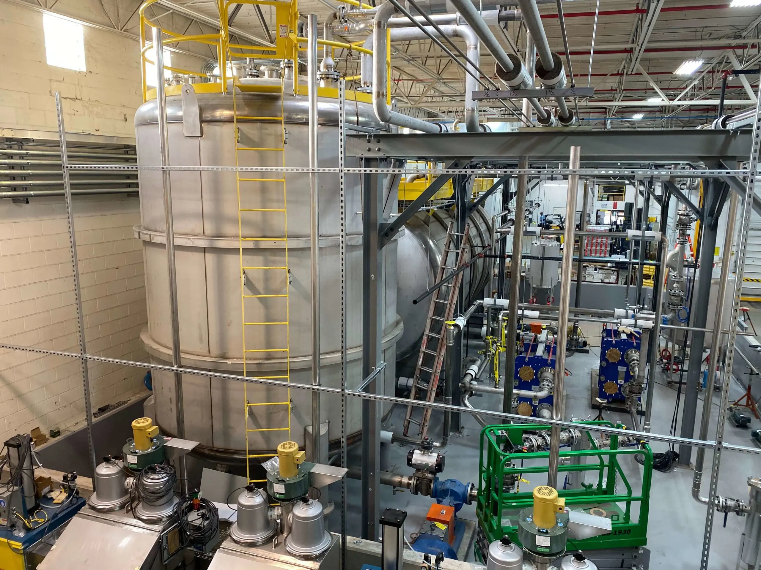 Industrial process tanks, pumps, and overhead piping inside a manufacturing facility