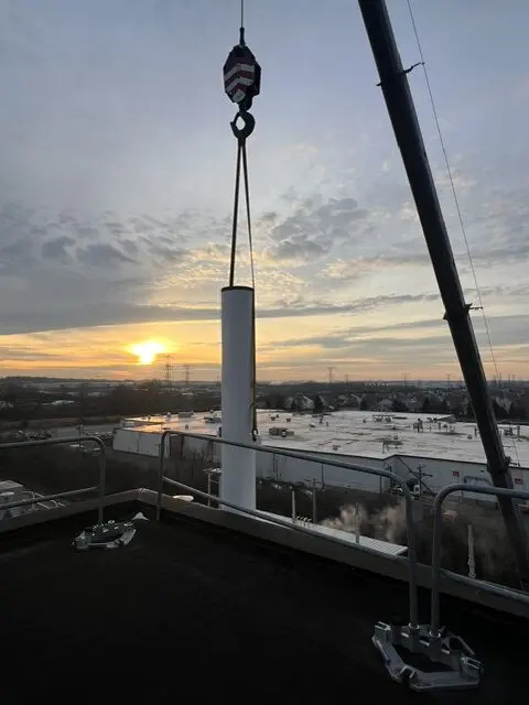 Crane lifting vertical industrial exhaust stack onto rooftop at chemical process facility