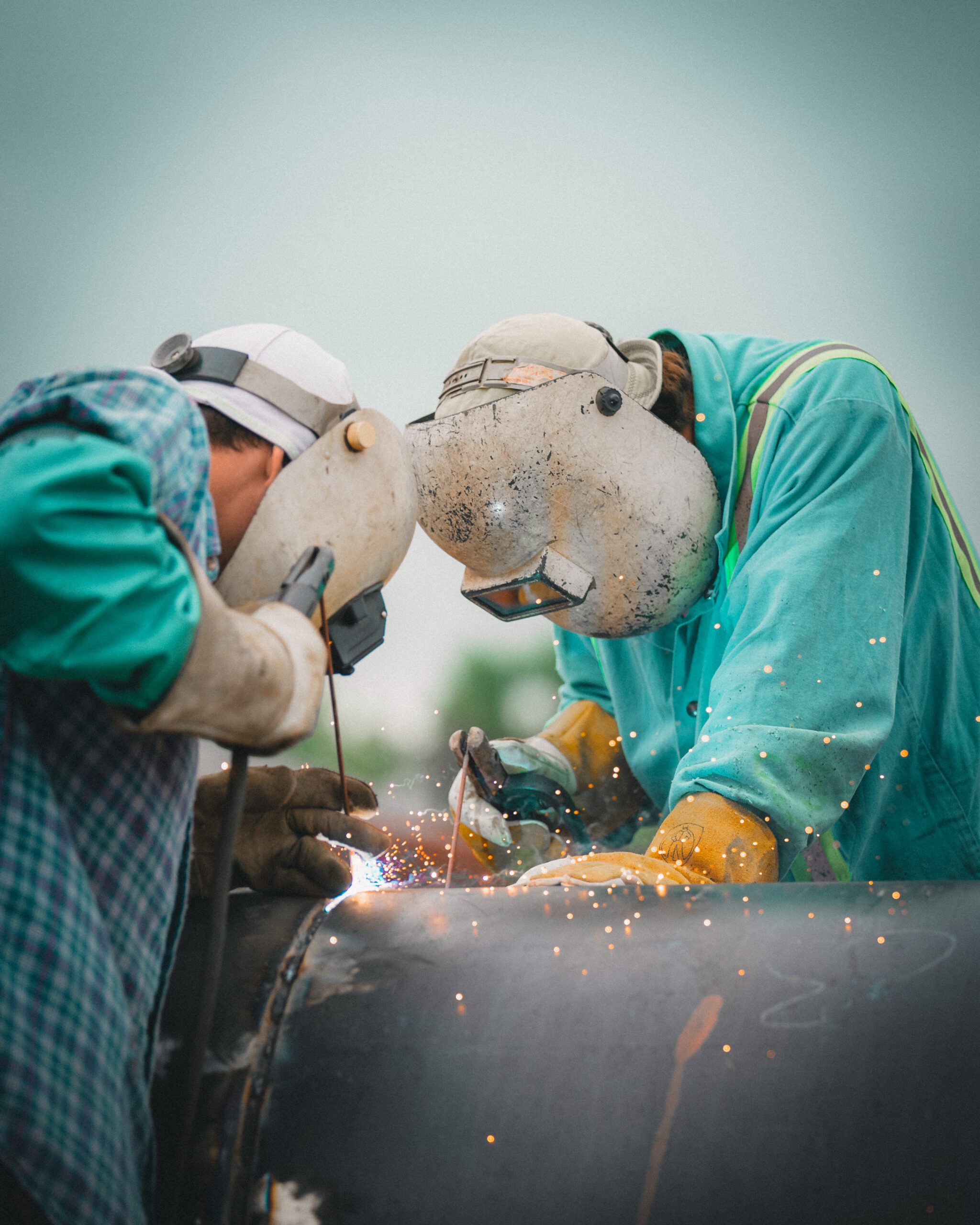 Two industrial welders performing field welding on large-diameter pipe section during heavy piping installation