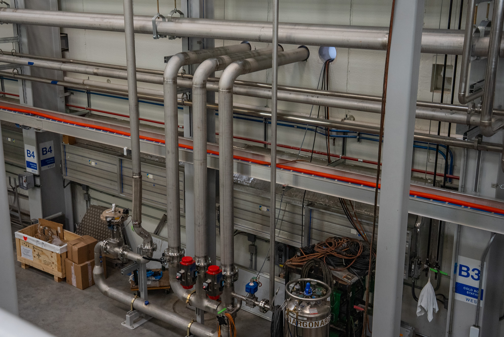 Interior industrial piping routed along a facility wall and down to floor-level equipment